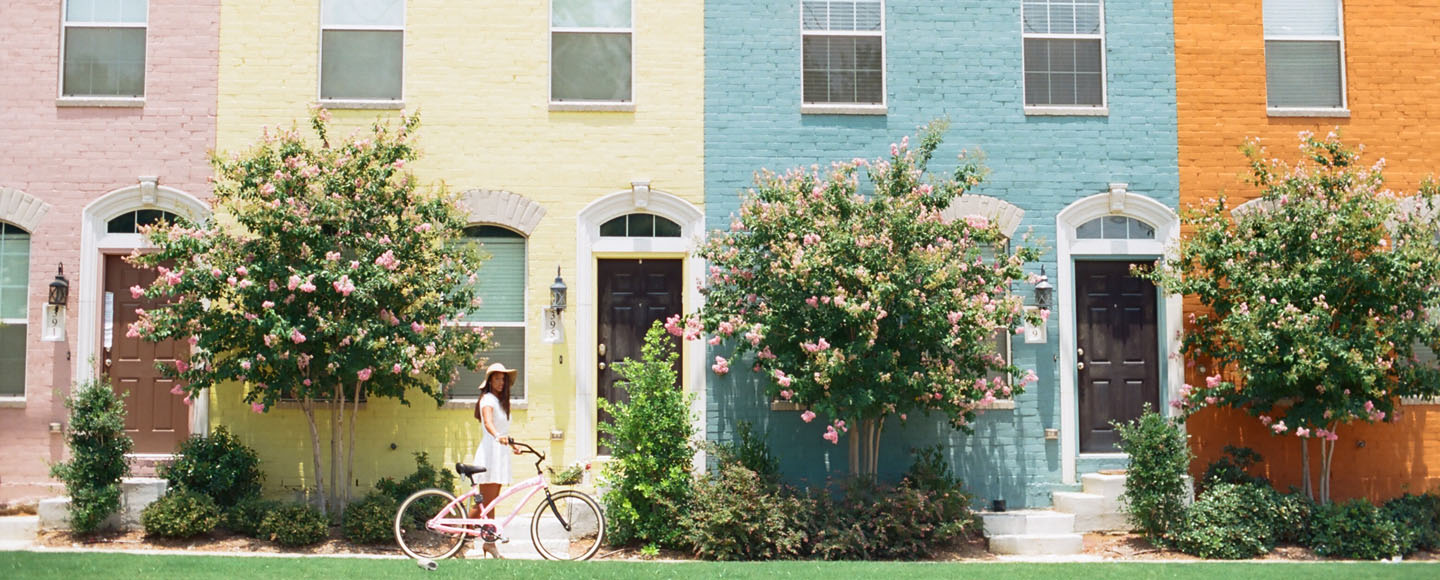 Dallas photographer captures senior pushing beach cruiser in front of colorful building.